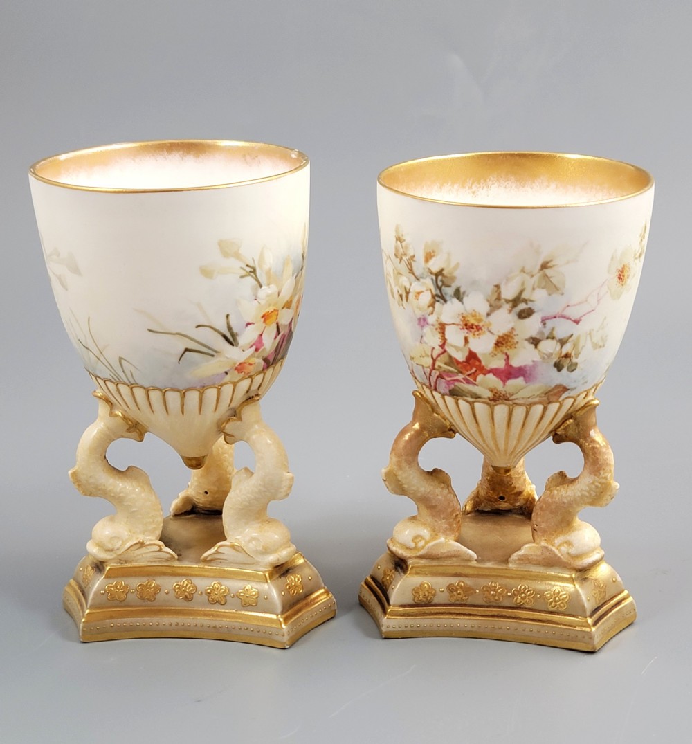 A pair of late Victorian Doulton Burslem porcelain beaker-form vases featuring hand-painted floral motifs and interior gilding, supported by three sculpted dolphin pedestals resting on moulded triangular gold bases. View III