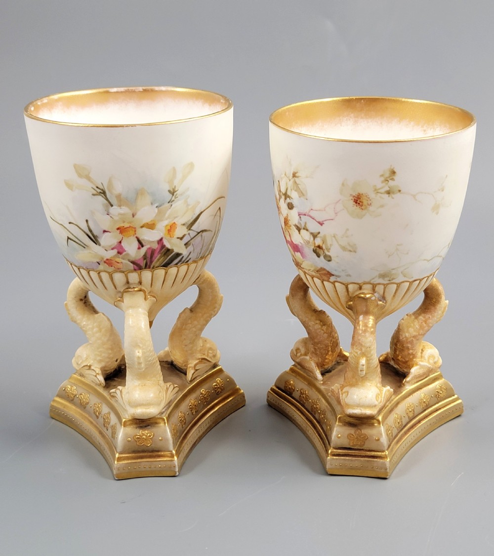 A pair of late Victorian Doulton Burslem porcelain beaker-form vases featuring hand-painted floral motifs and interior gilding, supported by three sculpted dolphin pedestals resting on moulded triangular gold bases. View IV