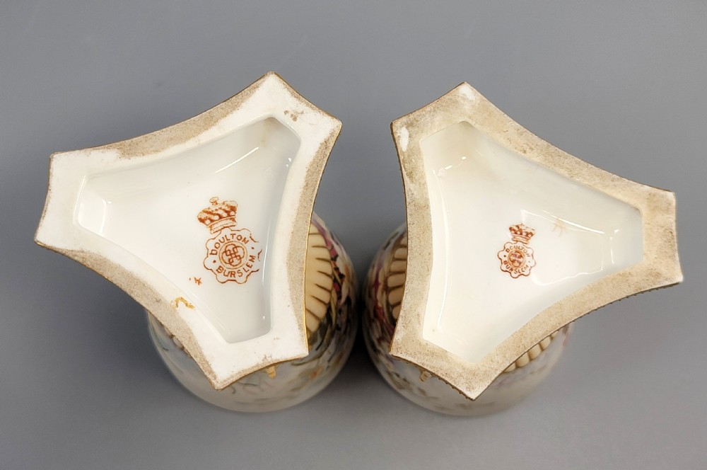 A pair of late Victorian Doulton Burslem porcelain beaker-form vases featuring hand-painted floral motifs and interior gilding, supported by three sculpted dolphin pedestals resting on moulded triangular gold bases. View VII
