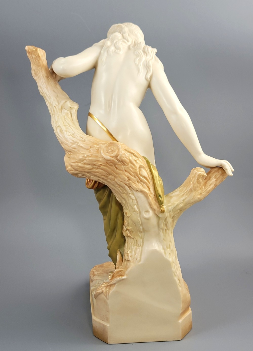 An Edwardian Royal Worcester porcelain figure depicting a classical female bather leaning against a tree trunk, rendered in cream porcelain with gold shot enamel drapery. View IV