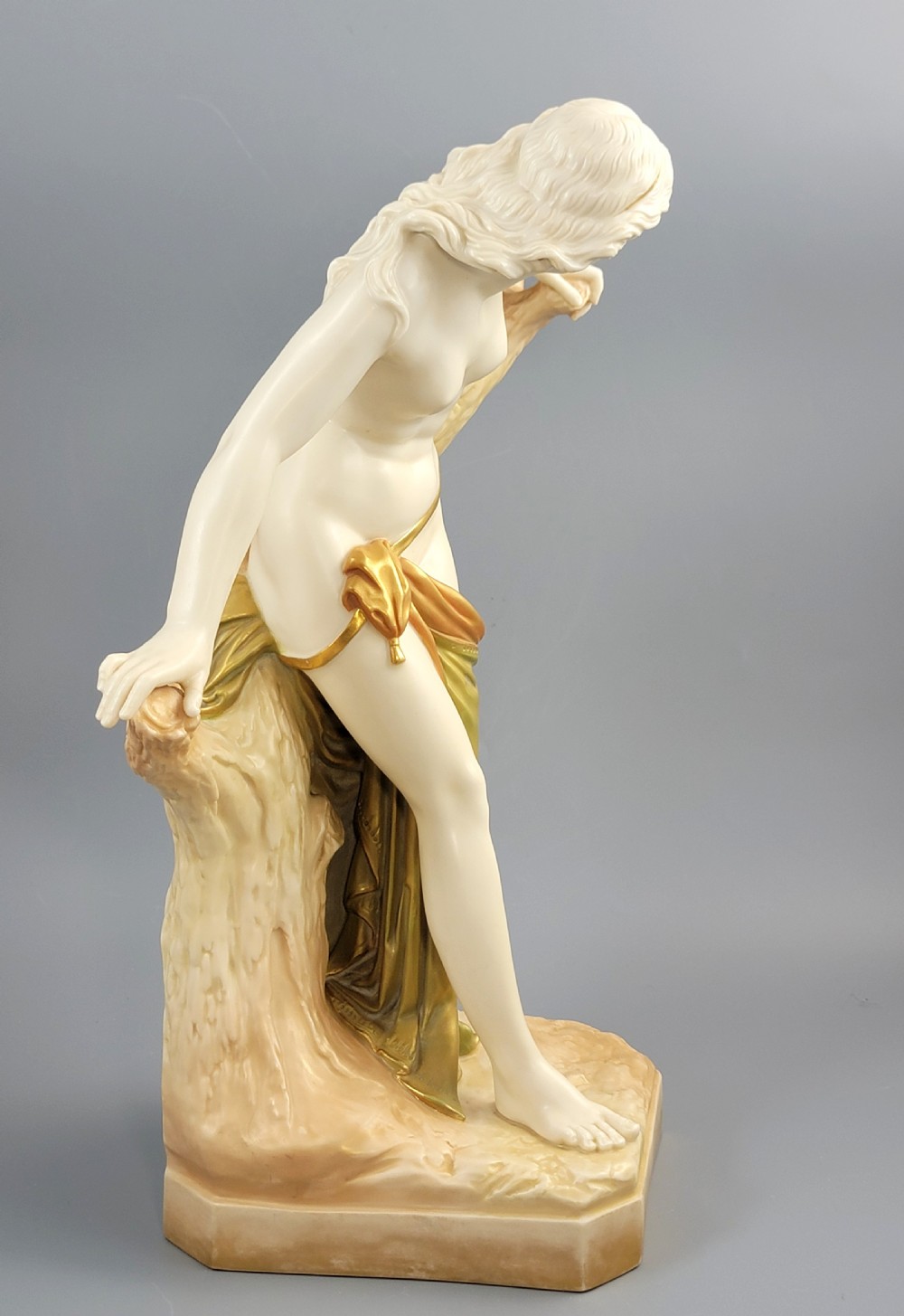 An Edwardian Royal Worcester porcelain figure depicting a classical female bather leaning against a tree trunk, rendered in cream porcelain with gold shot enamel drapery. View VI