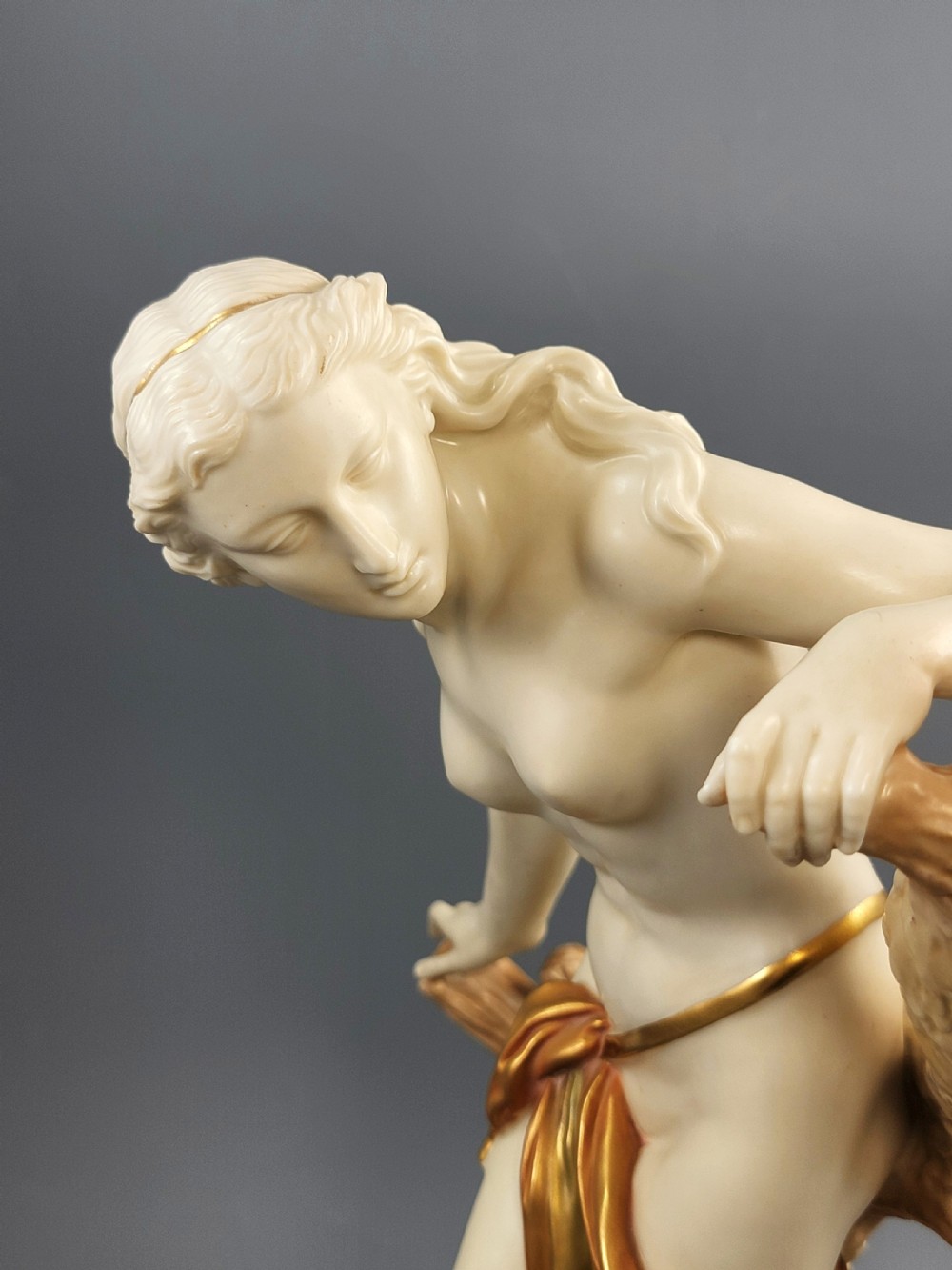 An Edwardian Royal Worcester porcelain figure depicting a classical female bather leaning against a tree trunk, rendered in cream porcelain with gold shot enamel drapery. View XI