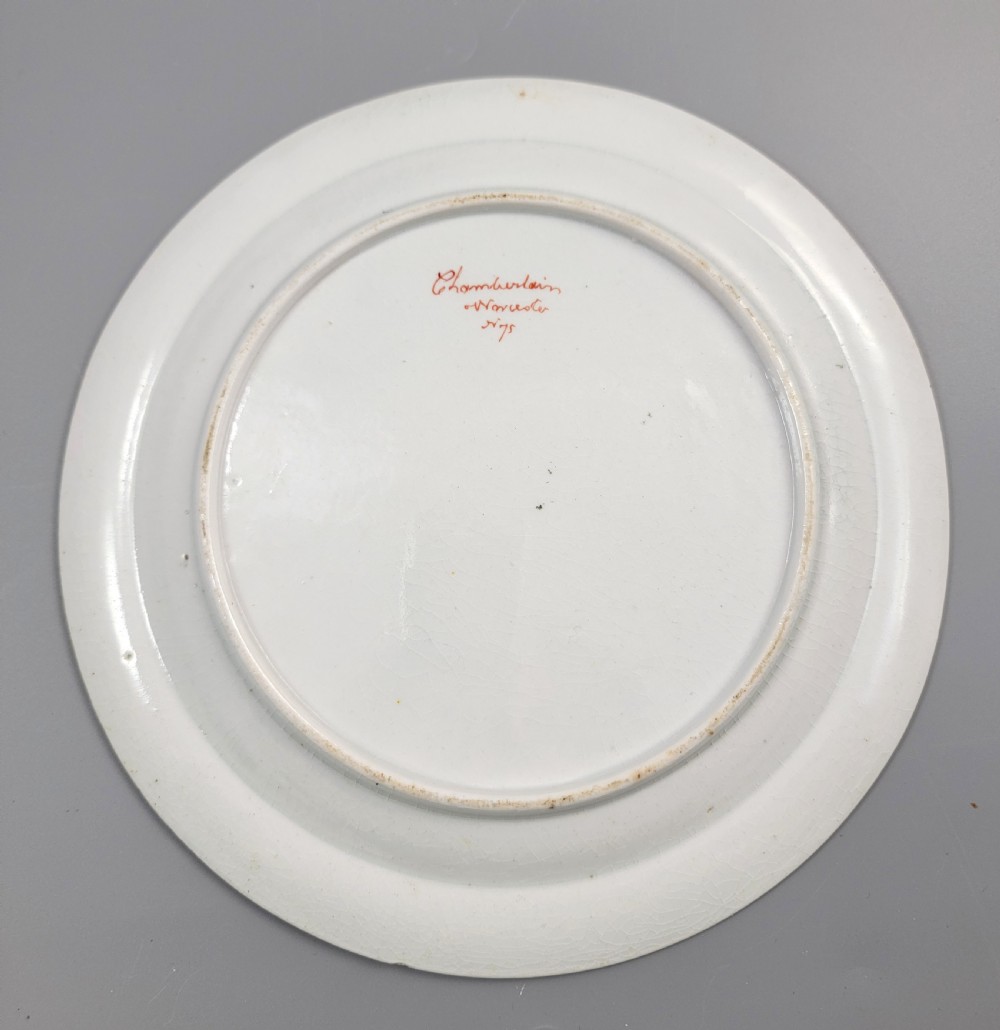 An antique circular porcelain dessert plate featuring hand-painted panels in red, green, and blue enamels surrounding a central family heraldic coat of arms. View III
