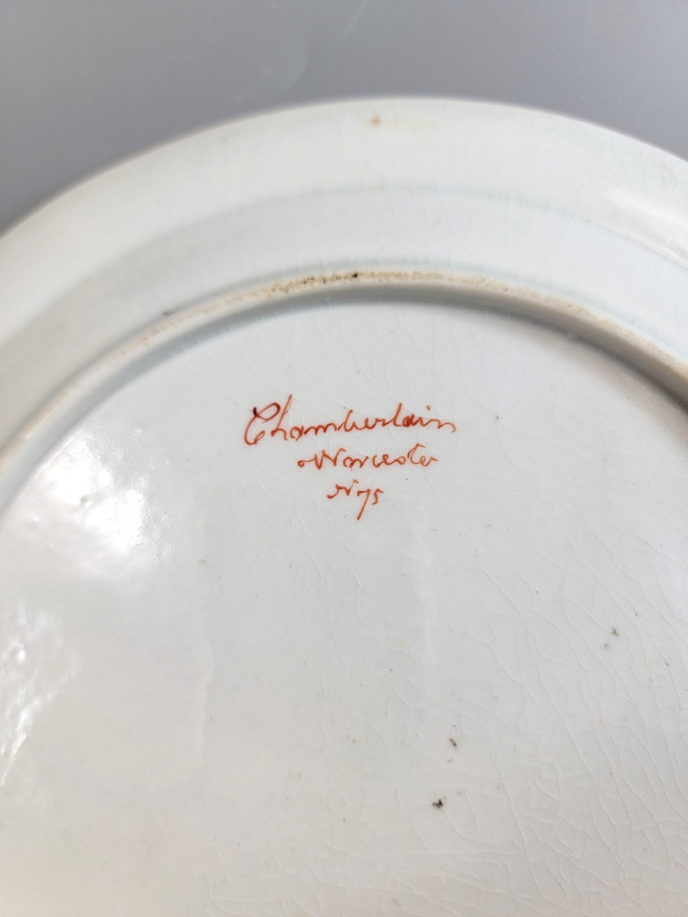 An antique circular porcelain dessert plate featuring hand-painted panels in red, green, and blue enamels surrounding a central family heraldic coat of arms. View IV