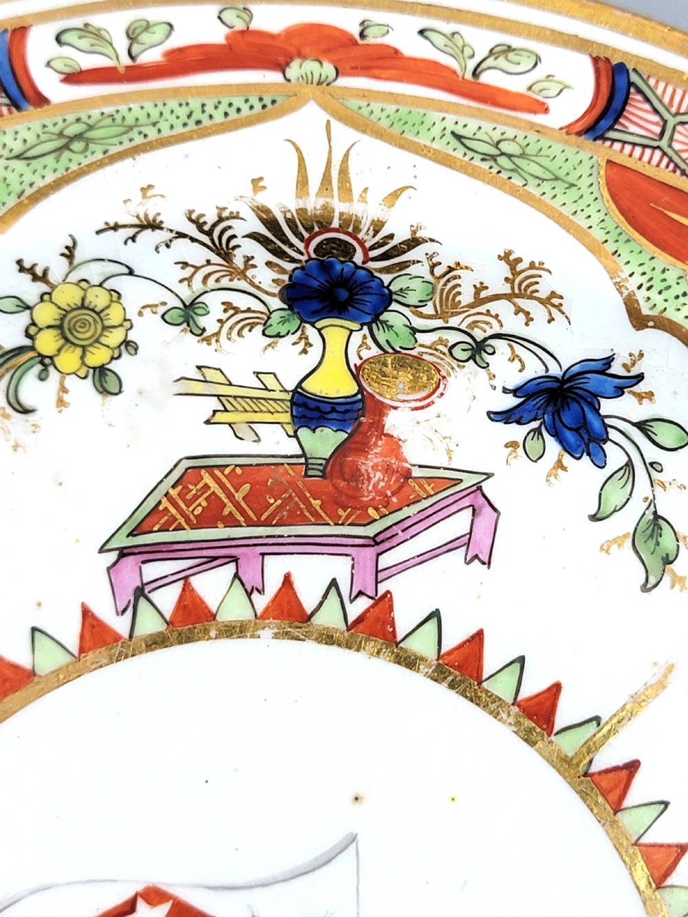 An antique circular porcelain dessert plate featuring hand-painted panels in red, green, and blue enamels surrounding a central family heraldic coat of arms. View VIII