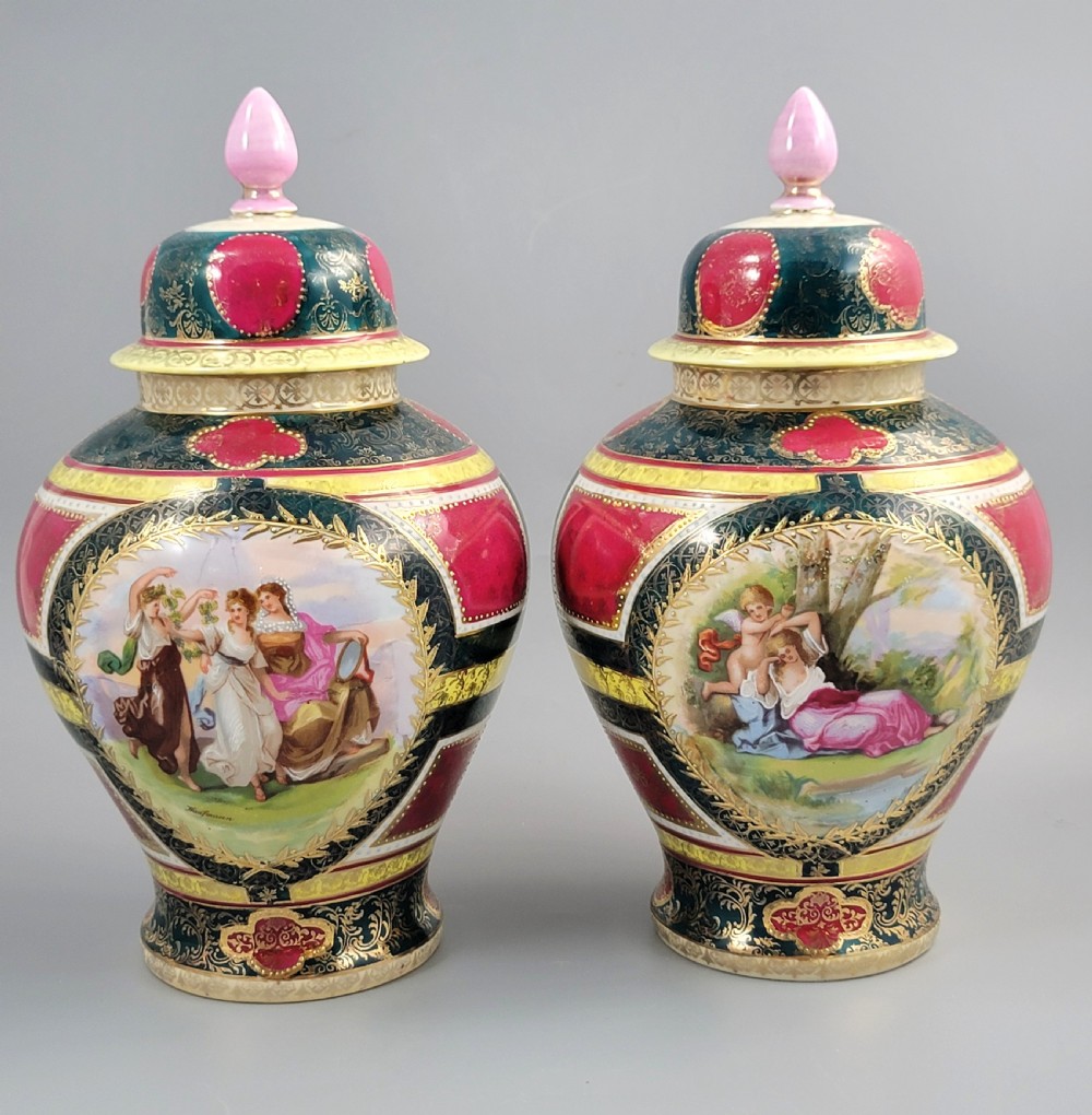 A pair of nineteenth-century Royal Vienna style porcelain covered urns featuring hand-painted classical figures inside oval gilt reserves, set against teal, pink, and yellow enamelled grounds.