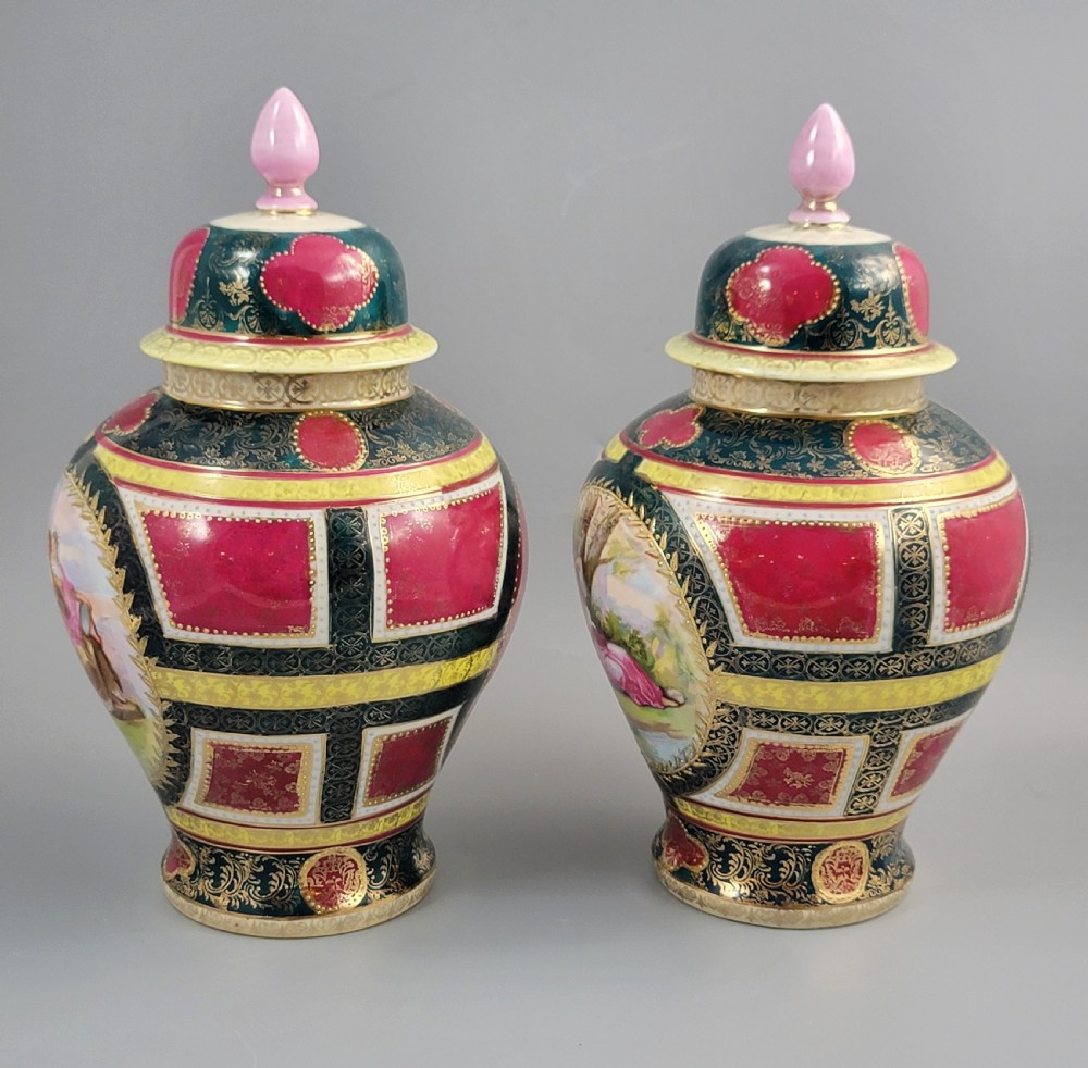 A pair of nineteenth-century Royal Vienna style porcelain covered urns featuring hand-painted classical figures inside oval gilt reserves, set against teal, pink, and yellow enamelled grounds. View II