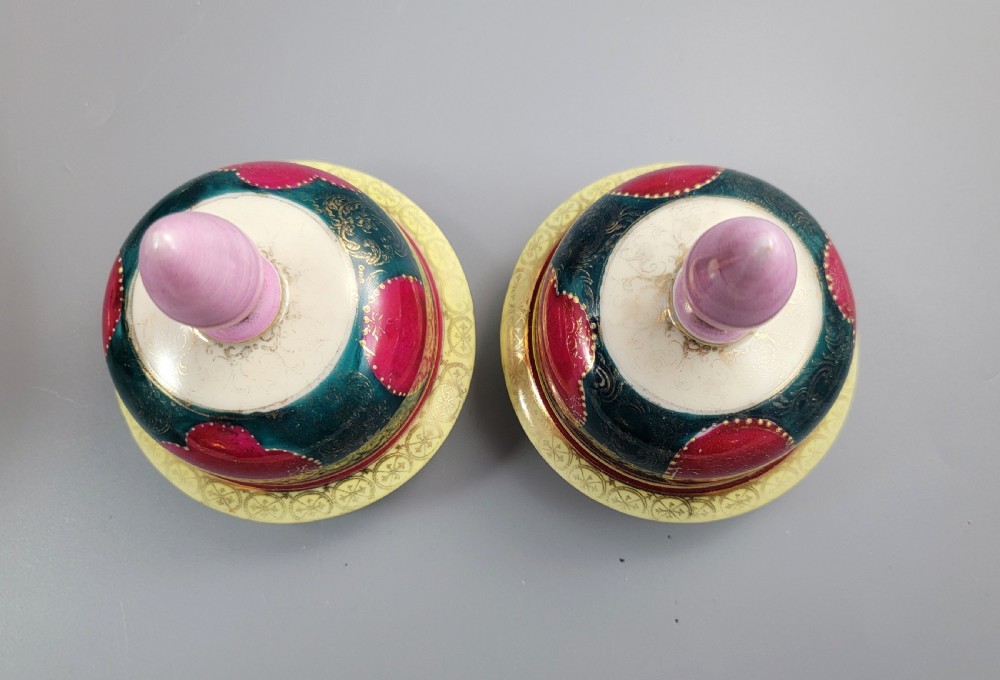 A pair of nineteenth-century Royal Vienna style porcelain covered urns featuring hand-painted classical figures inside oval gilt reserves, set against teal, pink, and yellow enamelled grounds. View X