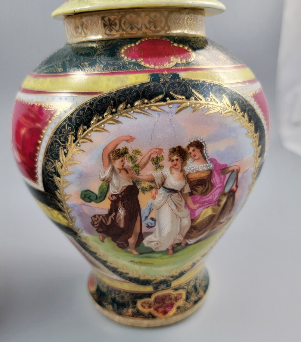 A pair of nineteenth-century Royal Vienna style porcelain covered urns featuring hand-painted classical figures inside oval gilt reserves, set against teal, pink, and yellow enamelled grounds. View XI