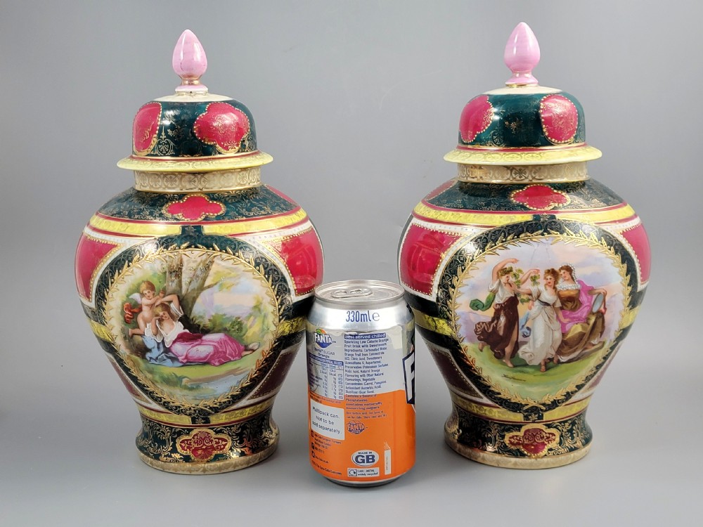 A pair of nineteenth-century Royal Vienna style porcelain covered urns featuring hand-painted classical figures inside oval gilt reserves, set against teal, pink, and yellow enamelled grounds. View XX