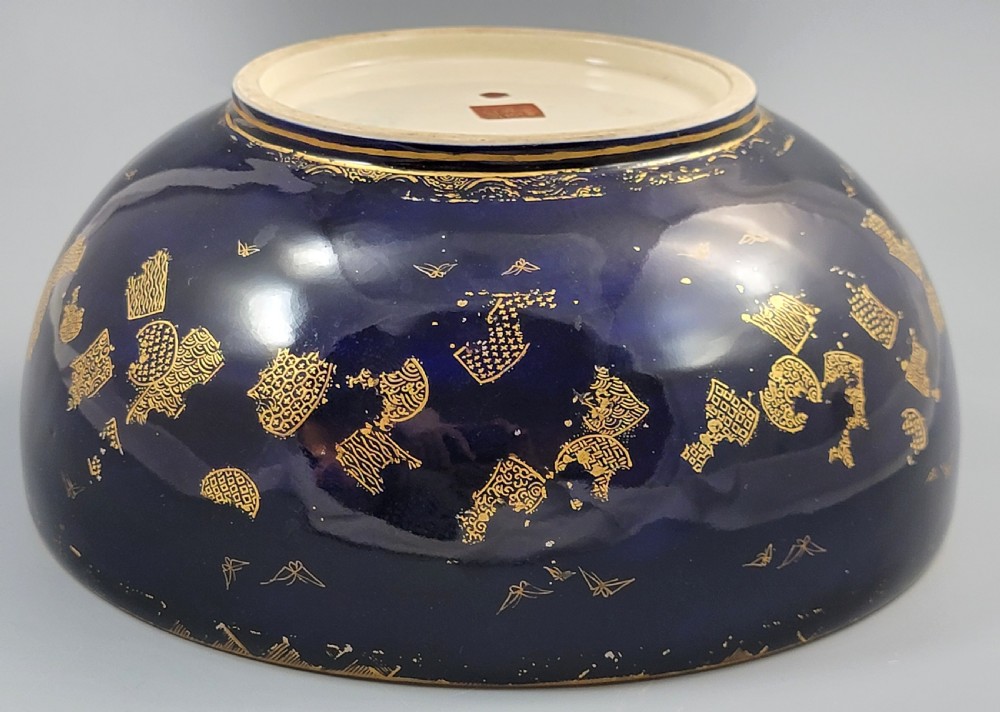 A circular Japanese Satsuma earthenware bowl featuring a central scene of samurai warriors in gold and polychrome enamels surrounded by a dark cobalt blue rim decorated with intricate gold scrollwork. View XII