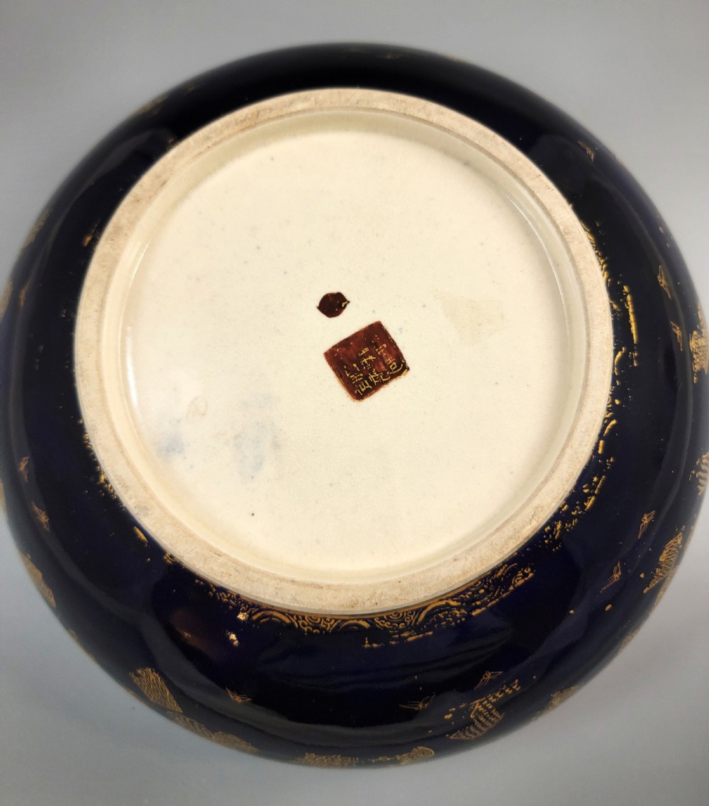 A circular Japanese Satsuma earthenware bowl featuring a central scene of samurai warriors in gold and polychrome enamels surrounded by a dark cobalt blue rim decorated with intricate gold scrollwork. View XIII