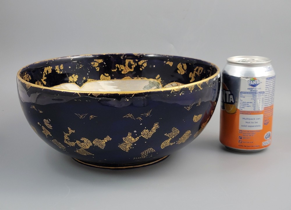 A circular Japanese Satsuma earthenware bowl featuring a central scene of samurai warriors in gold and polychrome enamels surrounded by a dark cobalt blue rim decorated with intricate gold scrollwork. View XV