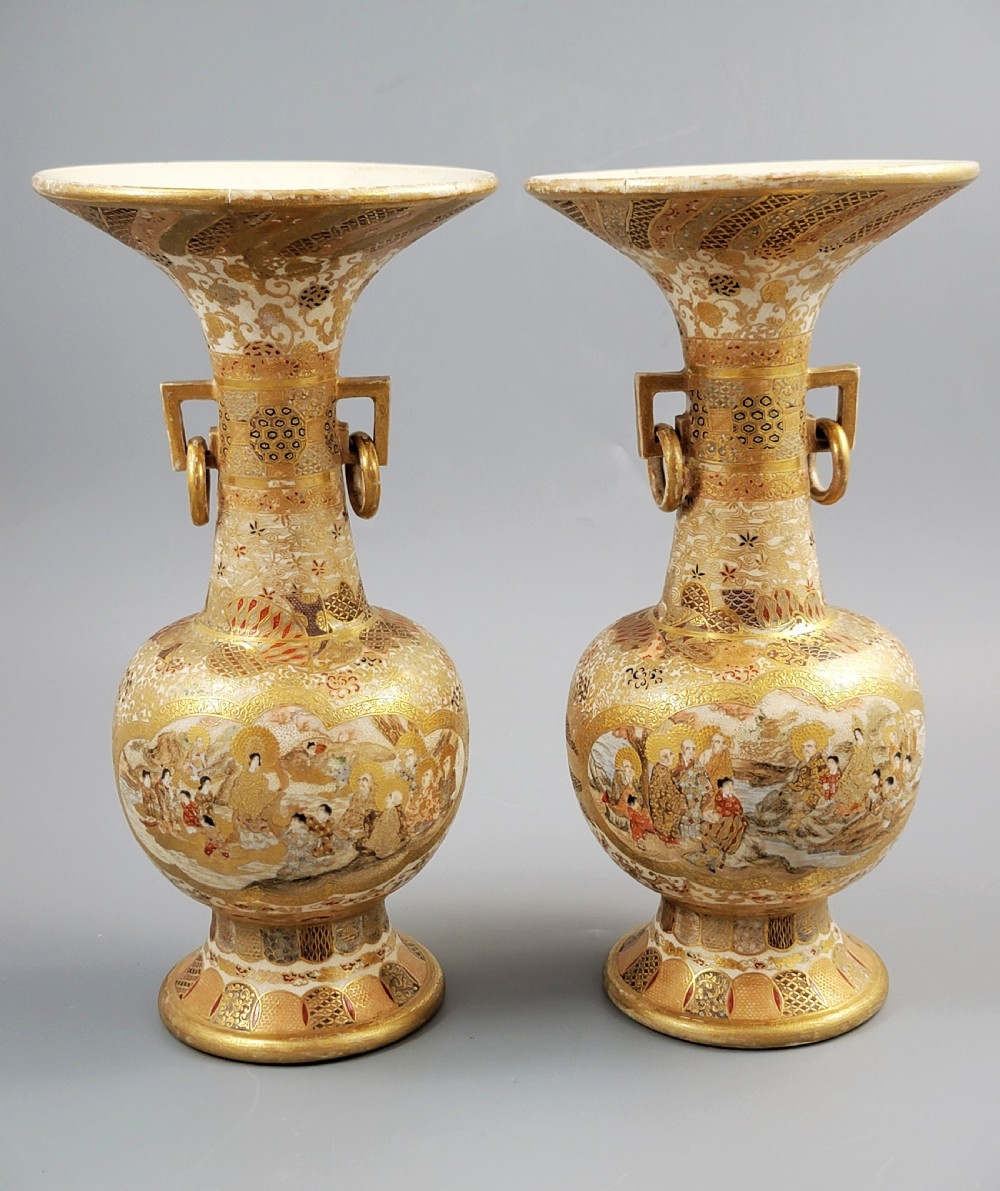 A pair of Japanese Satsuma earthenware vases featuring flared rims, fixed ring handles, and detailed hand-painted figural panels with extensive gold gilding.