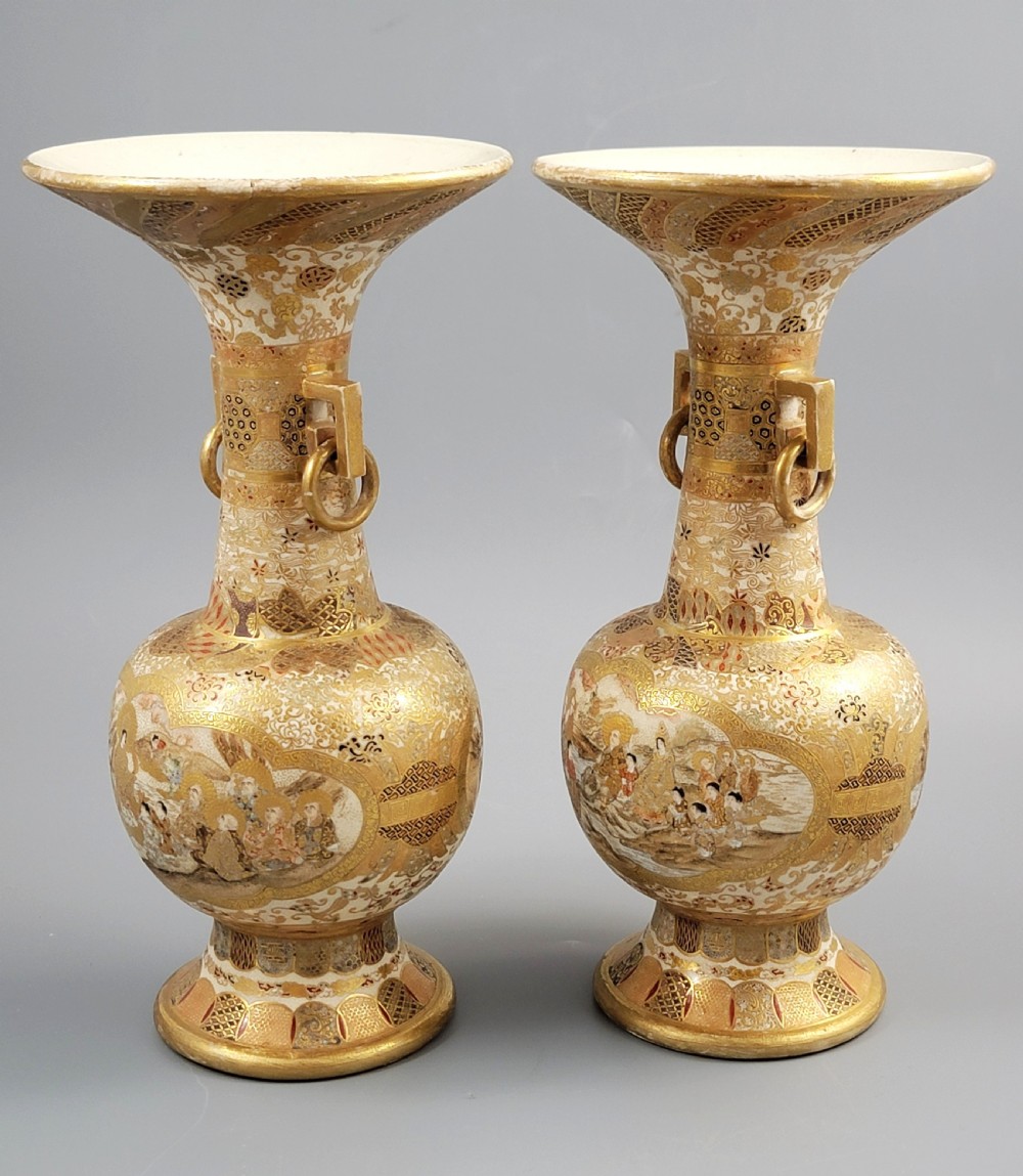 A pair of Japanese Satsuma earthenware vases featuring flared rims, fixed ring handles, and detailed hand-painted figural panels with extensive gold gilding. View II