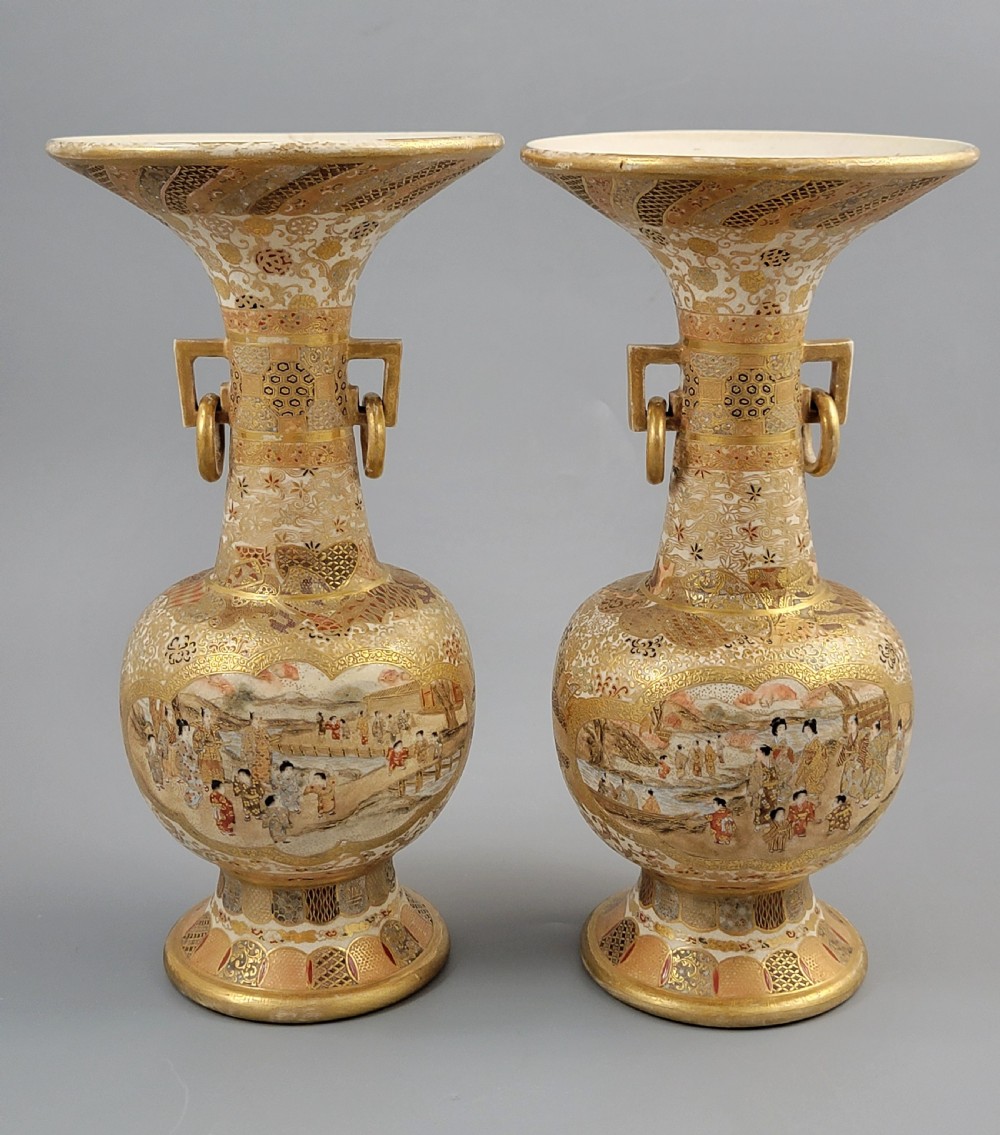 A pair of Japanese Satsuma earthenware vases featuring flared rims, fixed ring handles, and detailed hand-painted figural panels with extensive gold gilding. View V