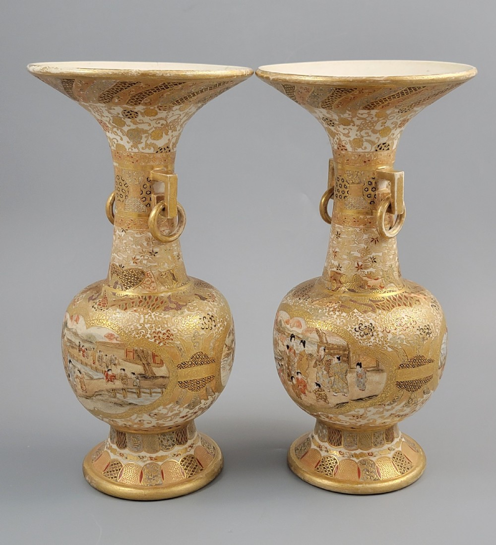 A pair of Japanese Satsuma earthenware vases featuring flared rims, fixed ring handles, and detailed hand-painted figural panels with extensive gold gilding. View VI