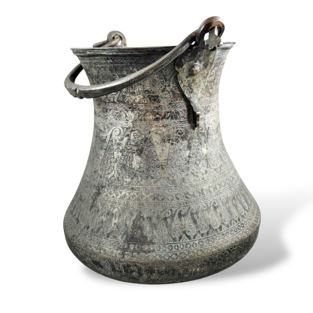 An 18th-century Persian engraved bronze ritual vessel featuring repeating boteh patterns, a flared upper rim, and a curved metal swing handle.