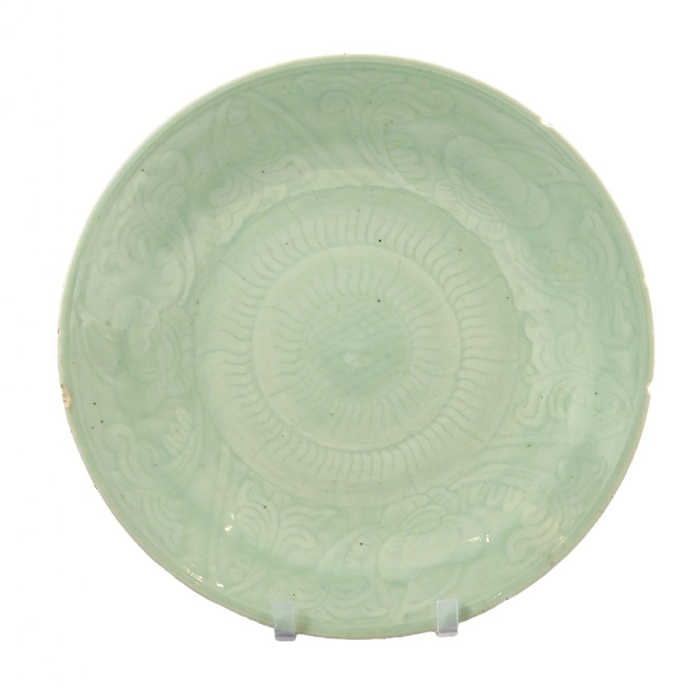 A circular Longquan celadon dish featuring a pale green glaze with moulded floral scrollwork and central radiating fluted details.