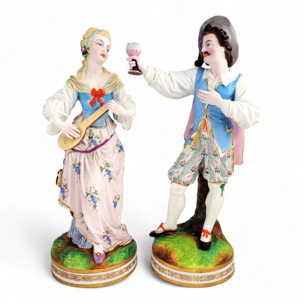 A pair of nineteenth-century French porcelain figurines depicting a man raising a glass and a woman playing a lute, dressed in pastel polychrome attire on gilded bases.