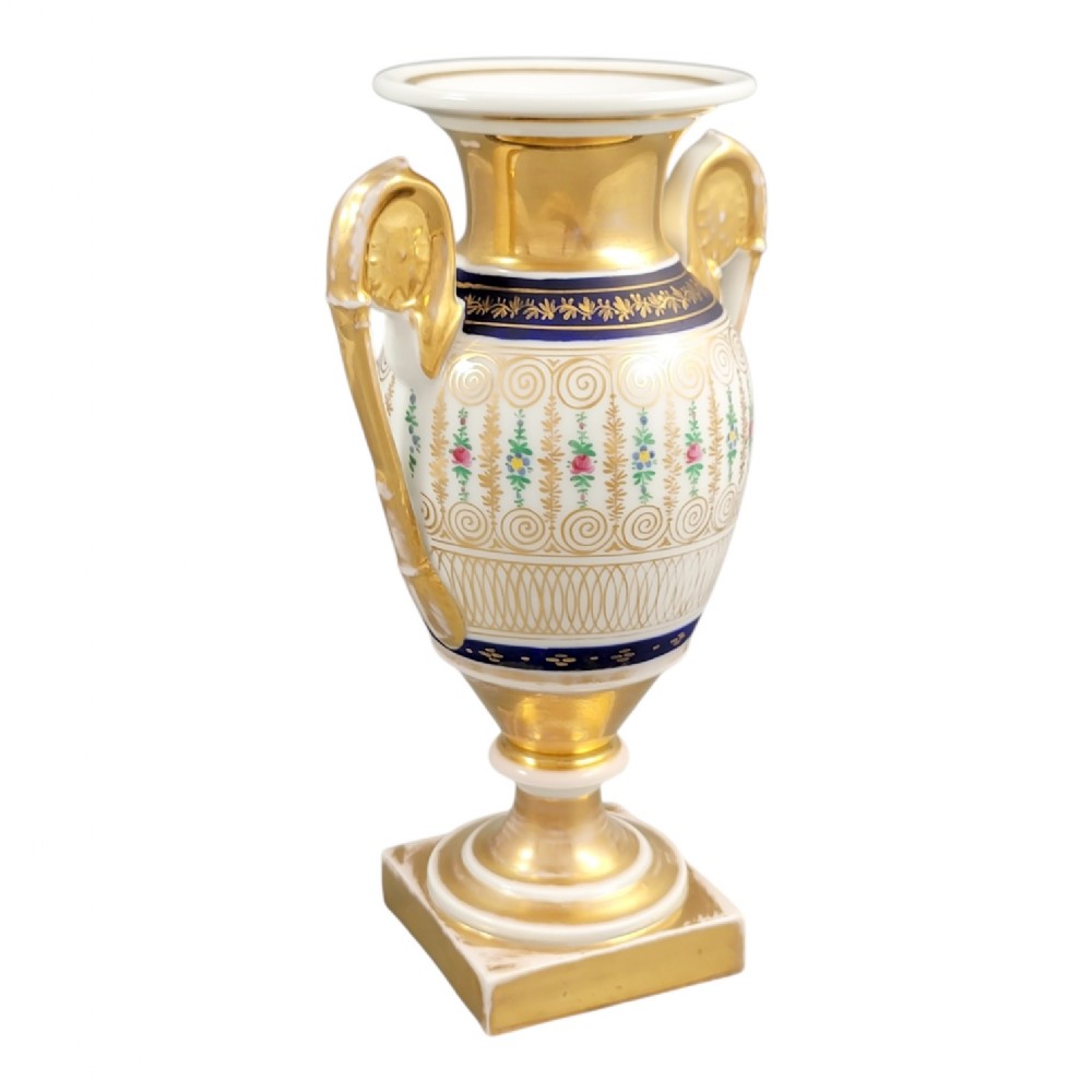 An antique French Empire style white porcelain urn featuring gilded scroll handles, polychrome floral decoration, cobalt blue borders, and a gold pedestal base.