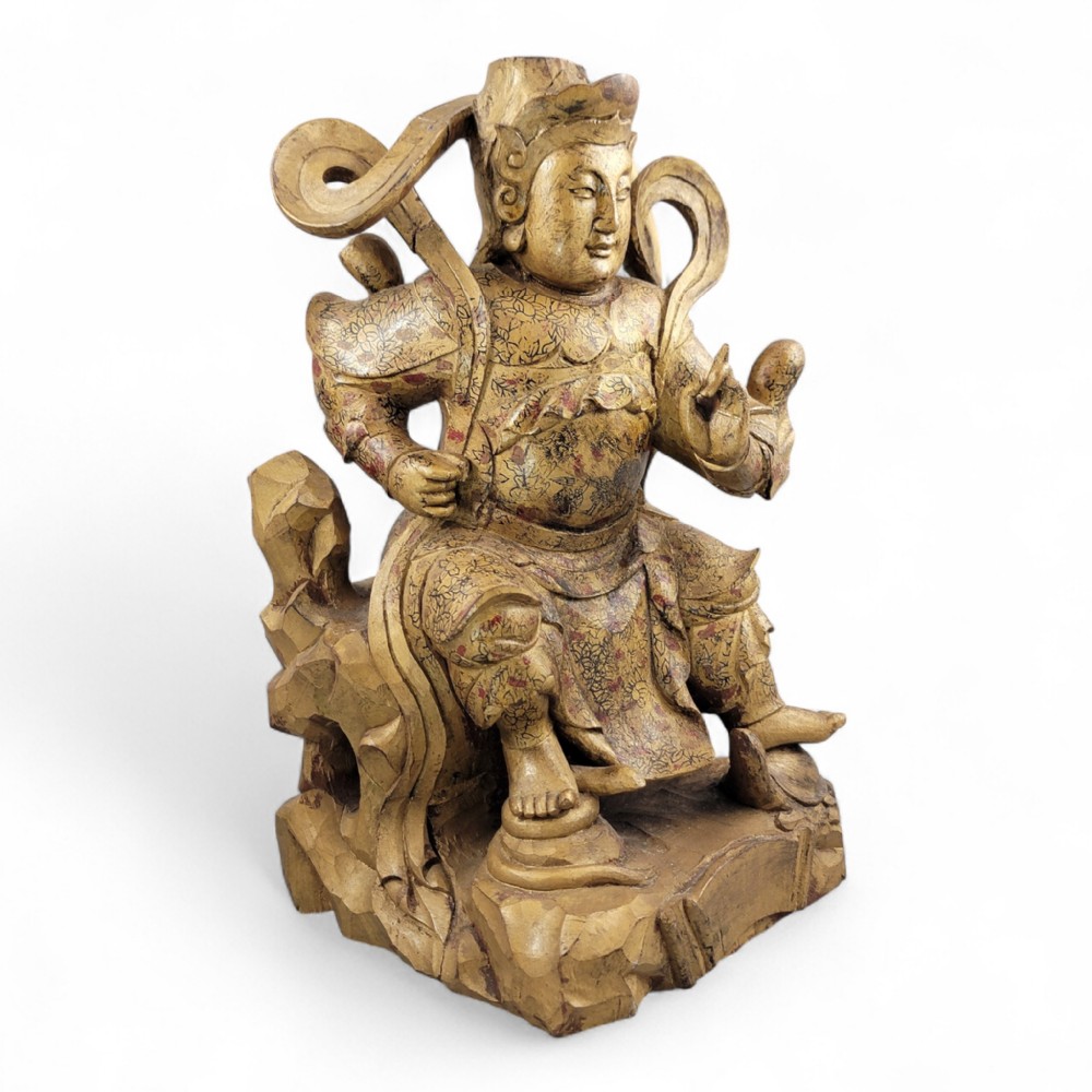 A 19th-century carved wooden Chinese temple guardian figure with intricate gilded and polychrome surface detail seated on a carved rocky base.