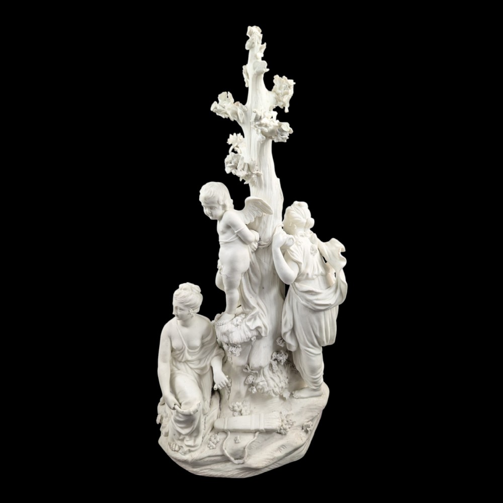 An 18th-century white unglazed biscuit porcelain figure group depicting the Three Graces surrounding Cupid tied to a central tree trunk.