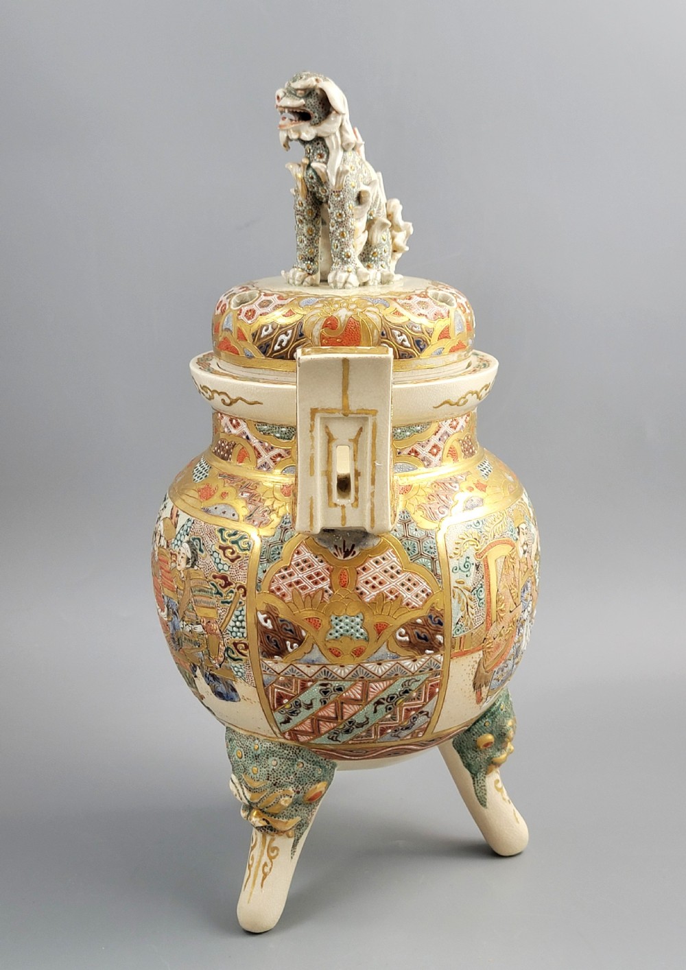 A cream-coloured Japanese Satsuma earthenware incense burner featuring a lid with a shishi lion finial, upright handles, tripod feet, and detailed polychrome paintings of samurai warriors with gold accents. View III
