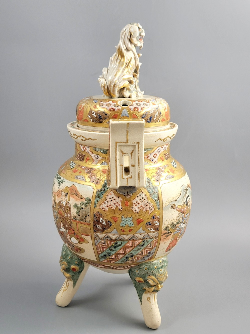 A cream-coloured Japanese Satsuma earthenware incense burner featuring a lid with a shishi lion finial, upright handles, tripod feet, and detailed polychrome paintings of samurai warriors with gold accents. View VII