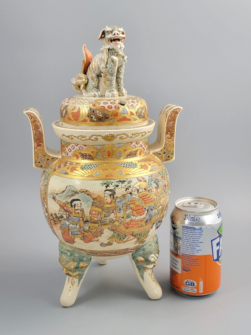 A cream-coloured Japanese Satsuma earthenware incense burner featuring a lid with a shishi lion finial, upright handles, tripod feet, and detailed polychrome paintings of samurai warriors with gold accents. View XVIII