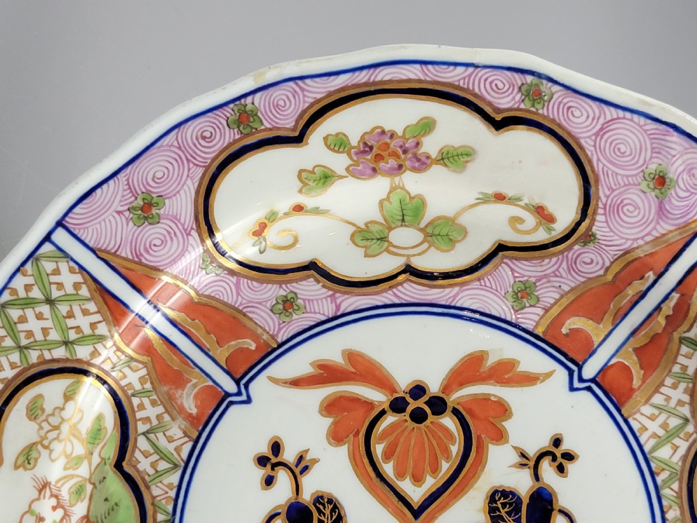 A pair of circular late 18th-century Derby porcelain plates featuring scalloped rims and hand-painted polychrome Kylin pattern designs in orange, cobalt blue, pink, and green. View V