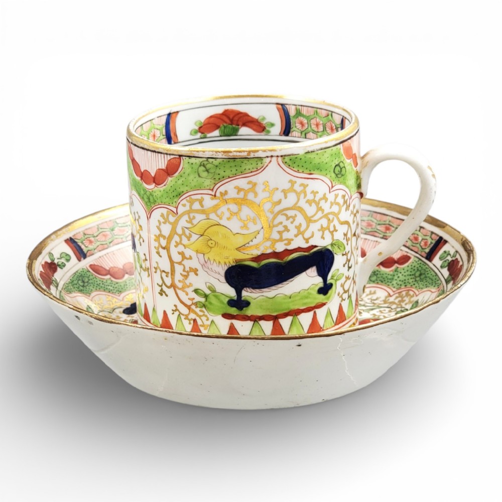 An antique Worcester porcelain coffee cup and deep saucer decorated with hand-painted Chinoiserie dragon motifs in green, red, yellow, and blue with gilded accents.