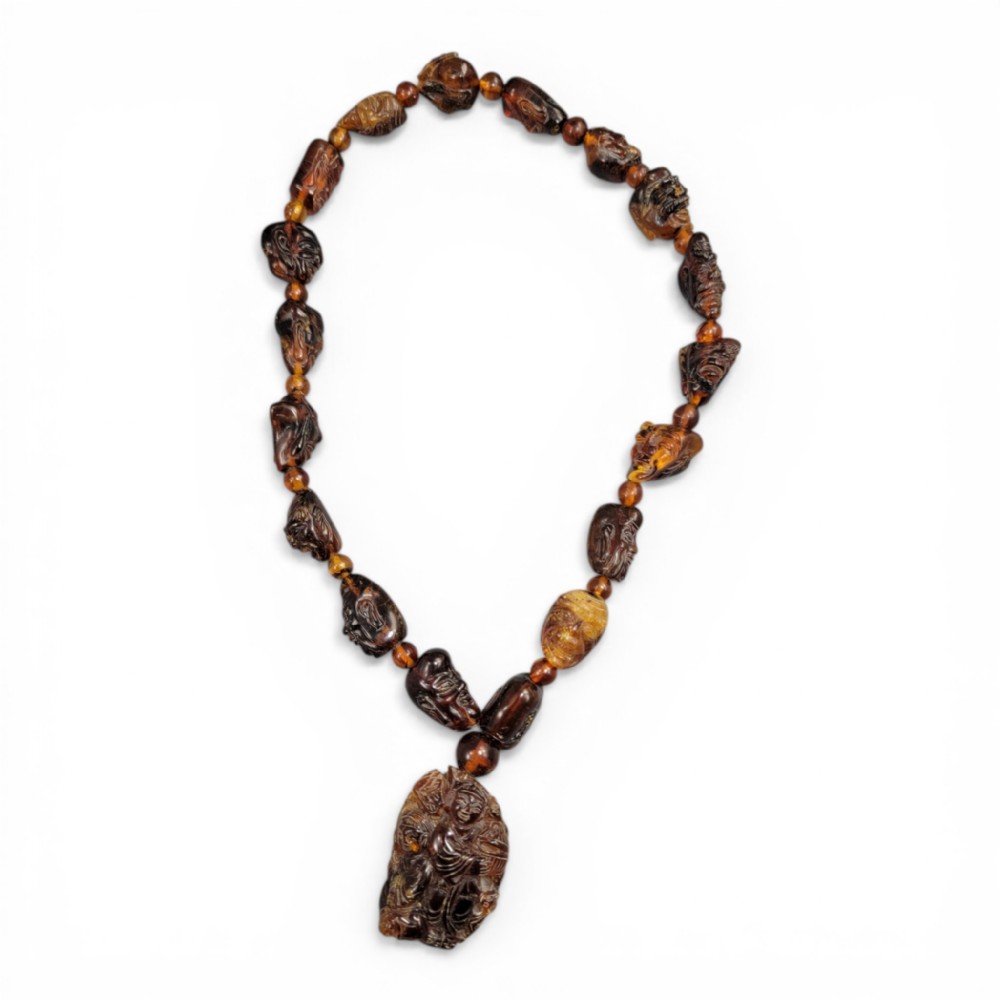 A Chinese amber necklace featuring eighteen hand-carved luohan head beads and a figural carved pendant drop.