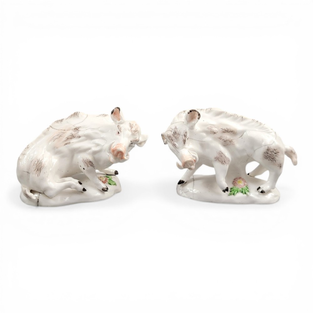 A pair of 18th-century off-white porcelain figures depicting wild boars with painted bristle details set on low naturalistic bases with small floral motifs.