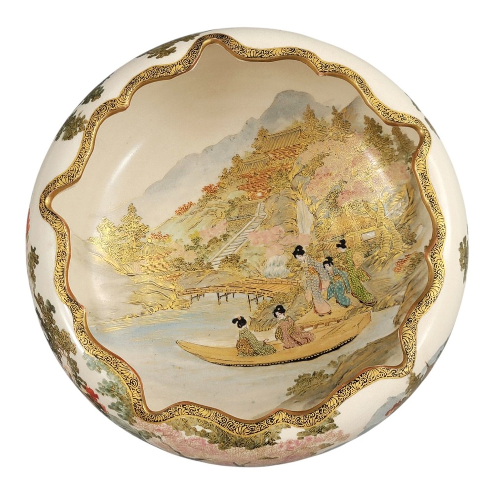 A Japanese Satsuma earthenware bowl with hand-painted figures under trees and gold accents, resting on a dark carved wooden stand. View II