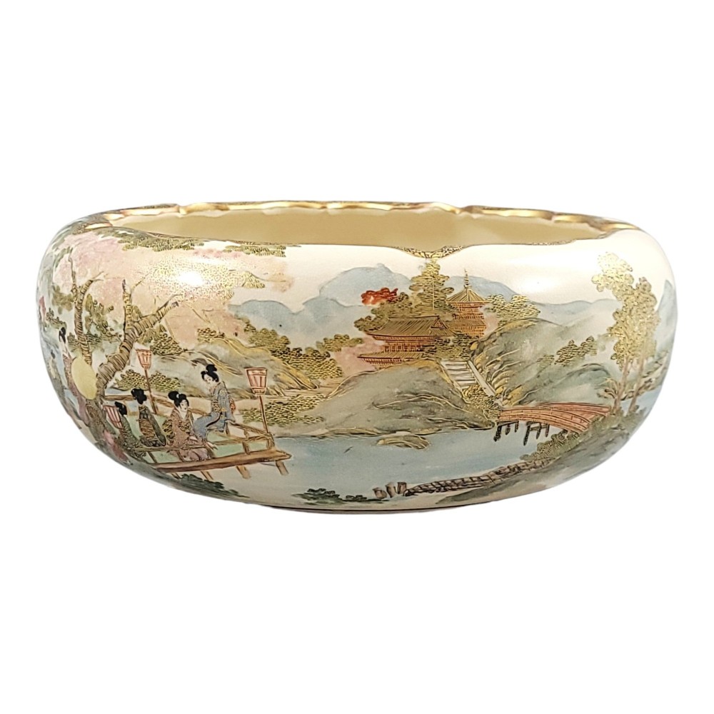 A Japanese Satsuma earthenware bowl with hand-painted figures under trees and gold accents, resting on a dark carved wooden stand. View VII