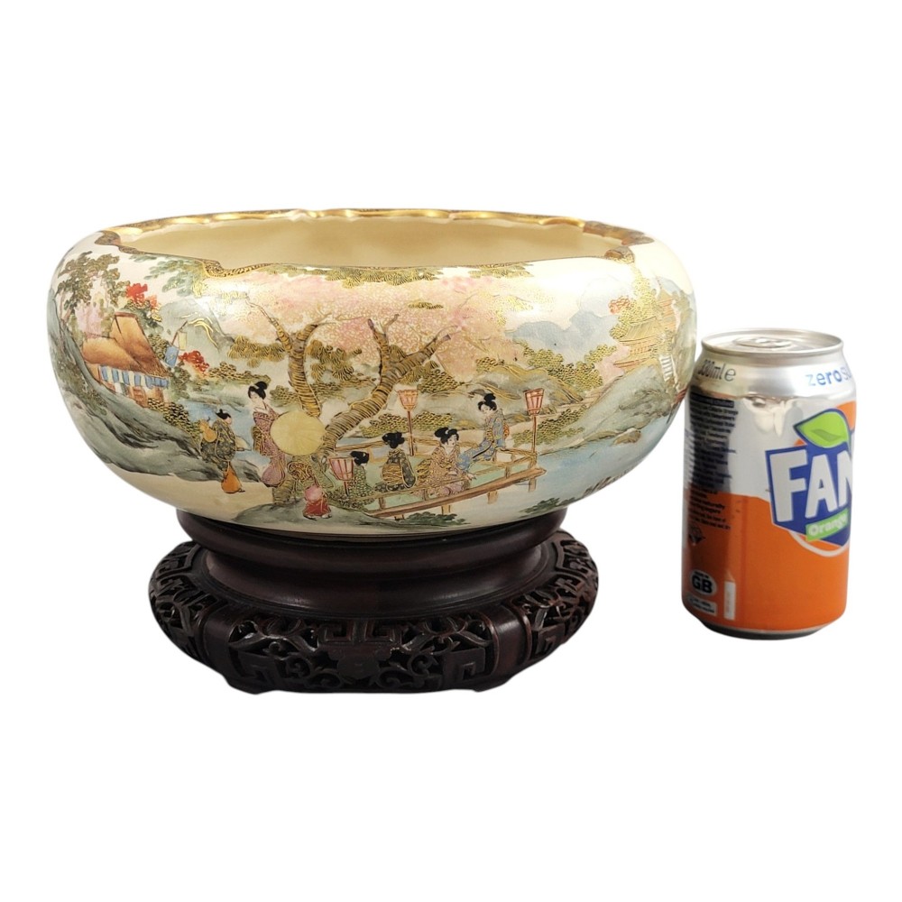 A Japanese Satsuma earthenware bowl with hand-painted figures under trees and gold accents, resting on a dark carved wooden stand. View XIII