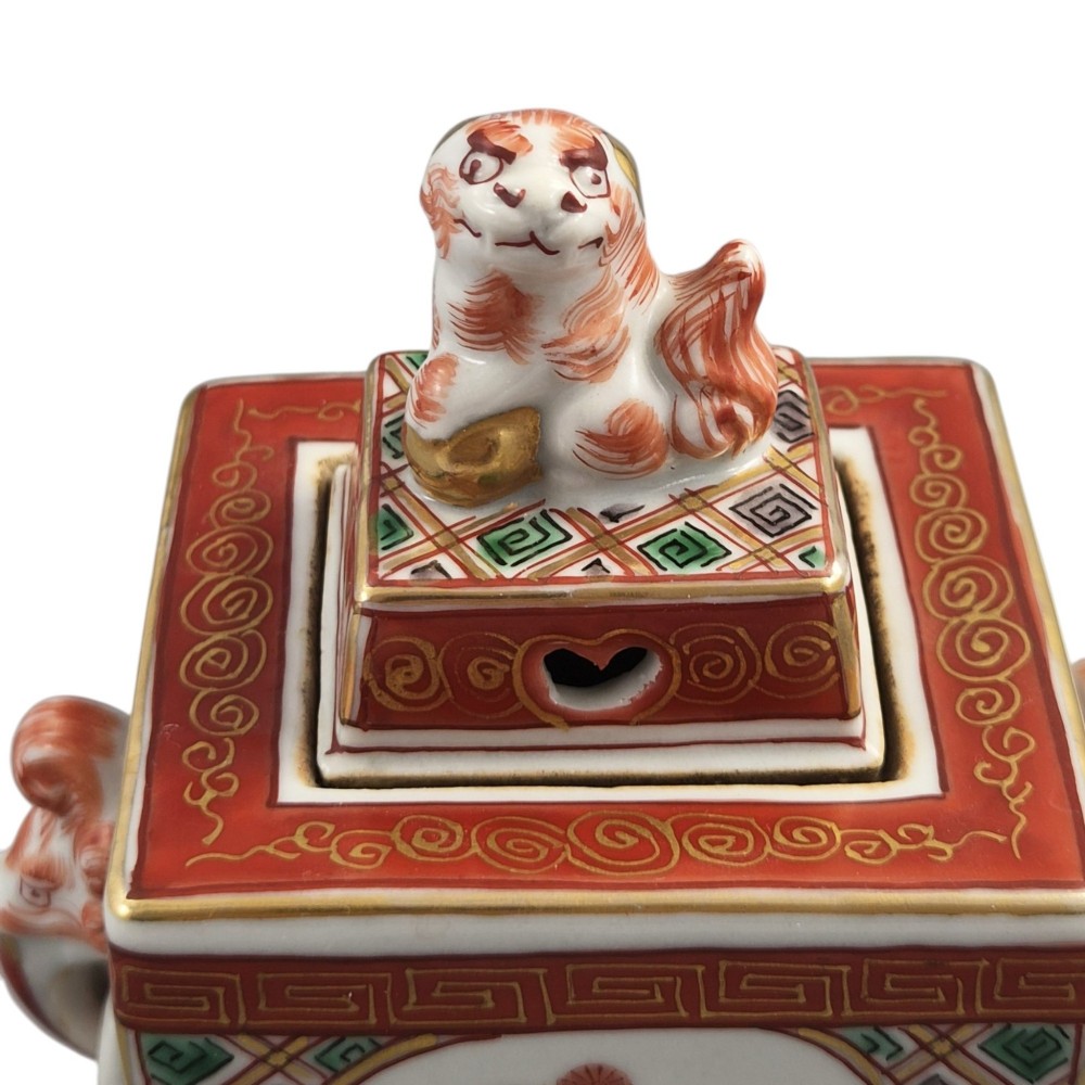 A rectangular Japanese porcelain incense burner featuring hand-painted depictions of a European ship, decorative red enamel borders, animal head handles, and a shishi lion finial on the lid. View V