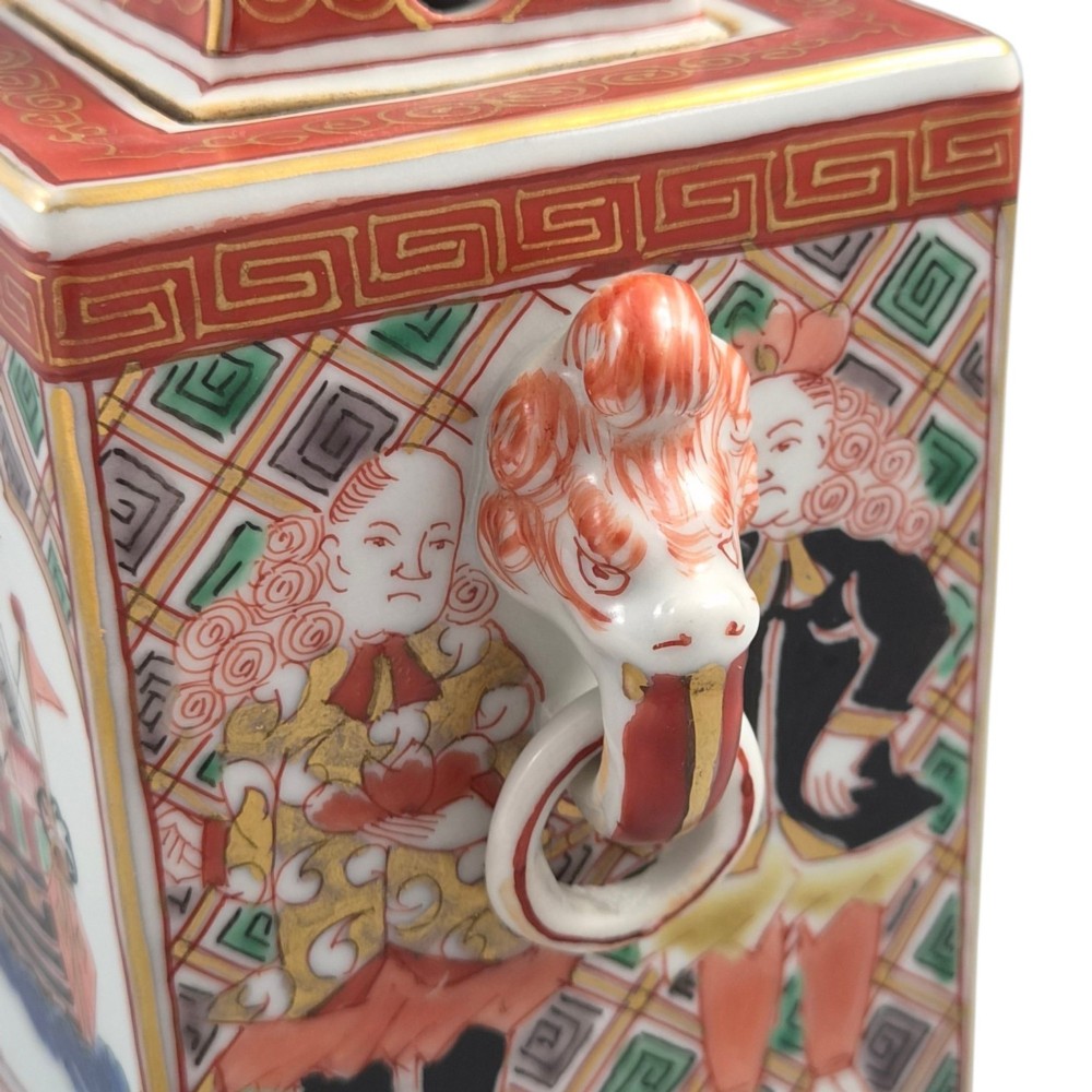 A rectangular Japanese porcelain incense burner featuring hand-painted depictions of a European ship, decorative red enamel borders, animal head handles, and a shishi lion finial on the lid. View VII