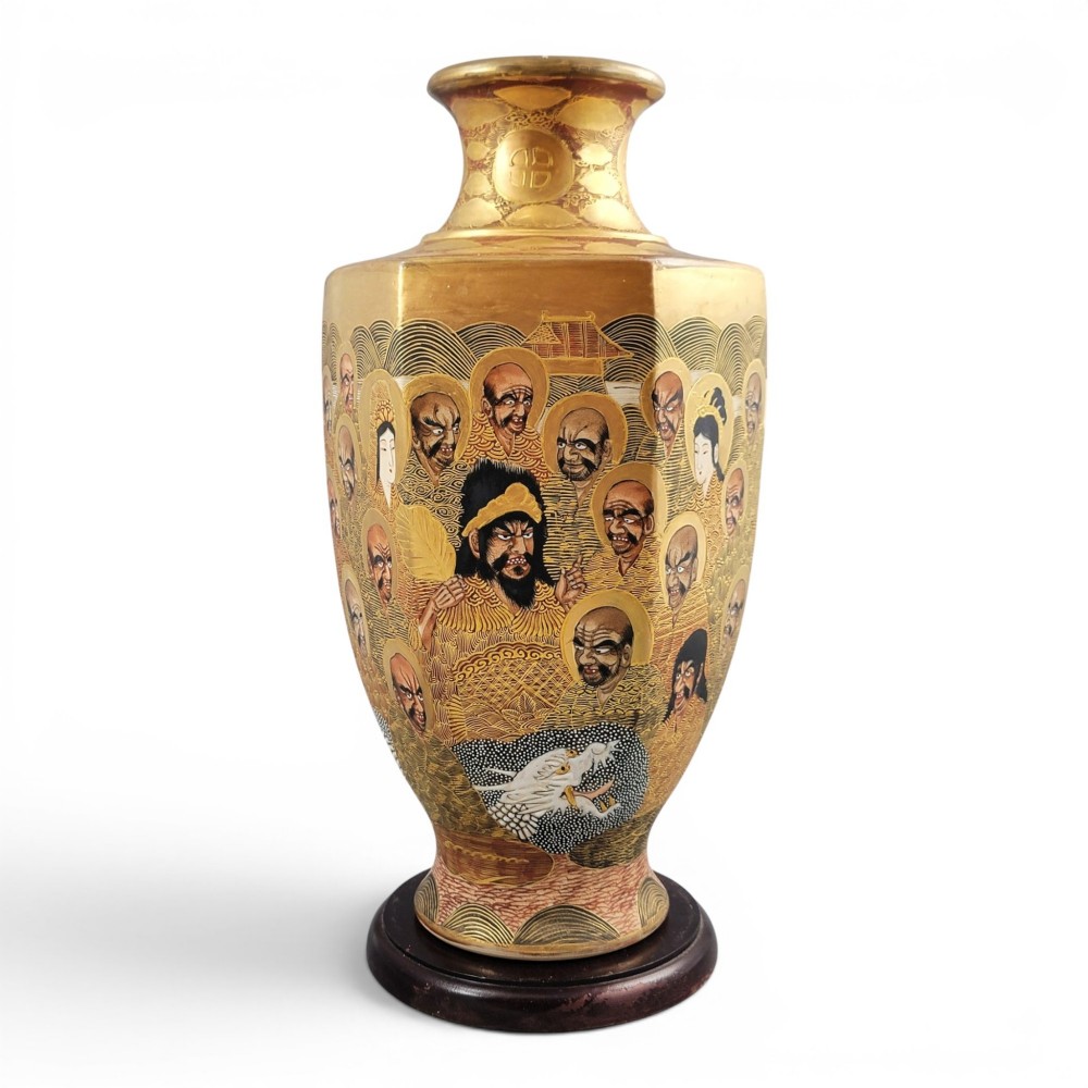 A tall gilded Japanese Satsuma earthenware vase painted with figures of Arhats and a dragon, set on a dark wooden base.