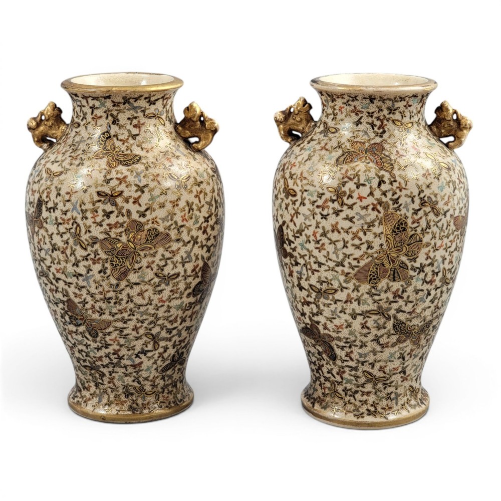 A pair of baluster-shaped Japanese Satsuma earthenware vases decorated with a dense pattern of polychrome butterflies and gold lion-dog side handles.