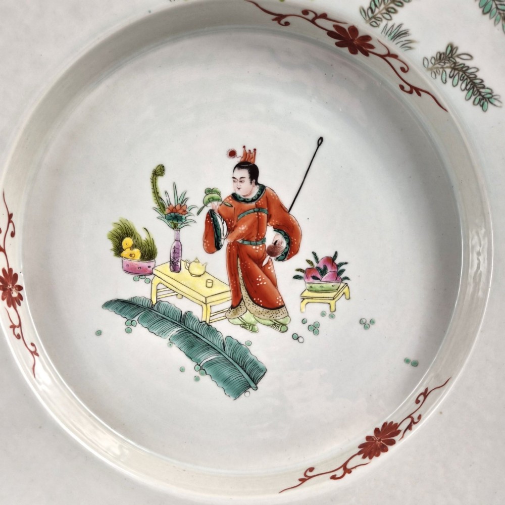 A late Qing dynasty Chinese Famille Rose porcelain dish featuring a hand-painted central figure, lotus blossoms, butterflies, and a distinct red castellated rim. View II