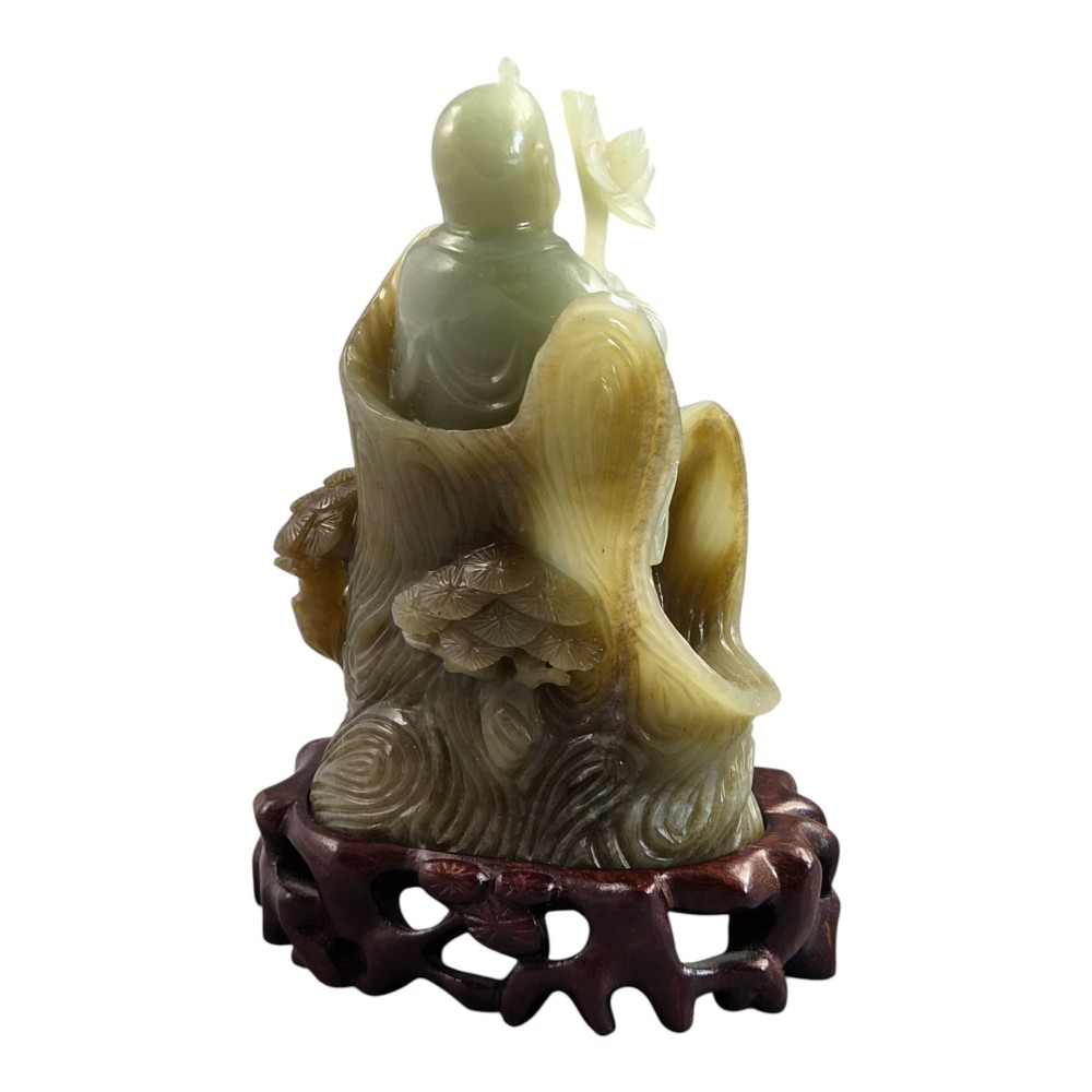 A carved pale green Chinese jadeite figure holding a lotus stem, resting on a fitted dark carved wooden stand. View V