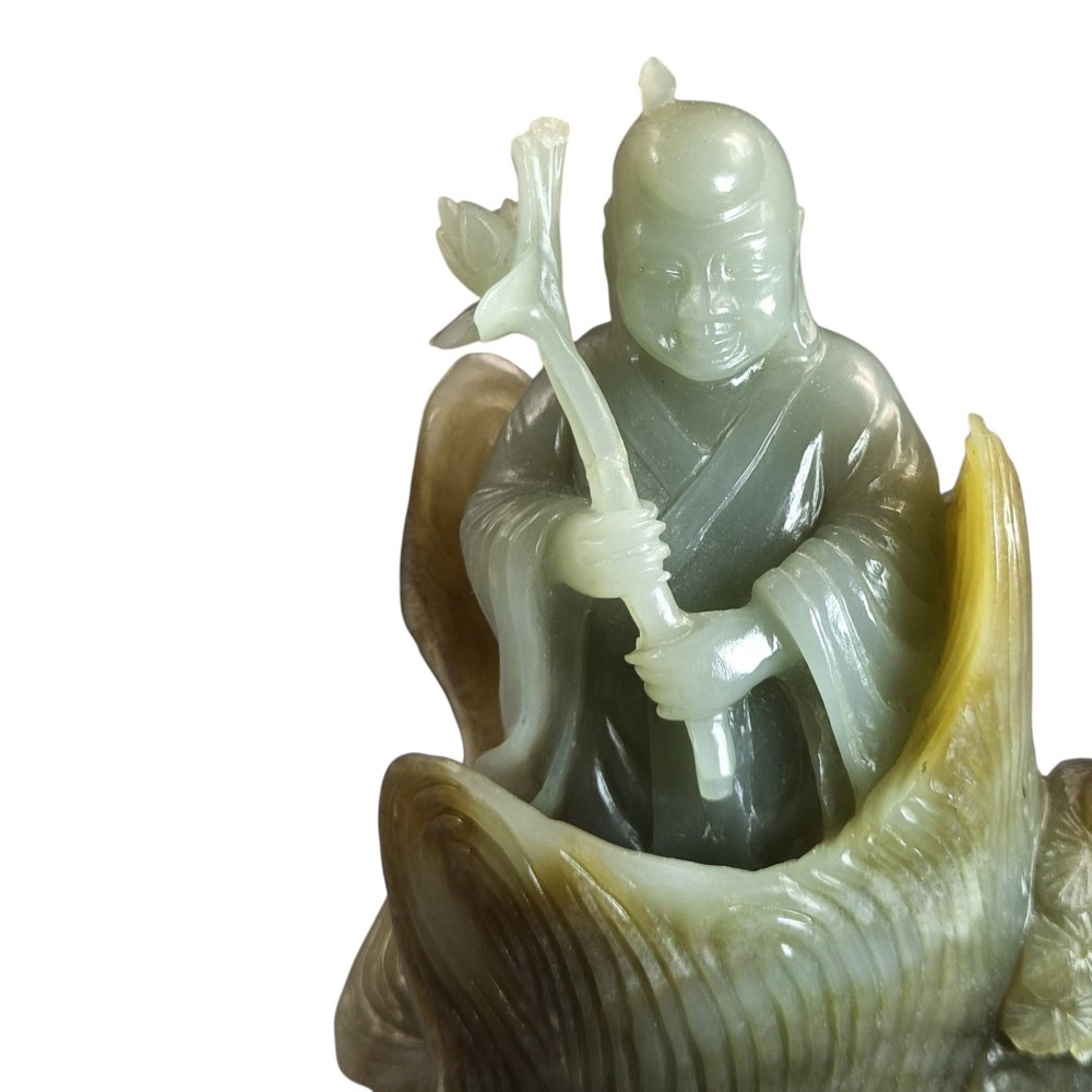 A carved pale green Chinese jadeite figure holding a lotus stem, resting on a fitted dark carved wooden stand. View VIII