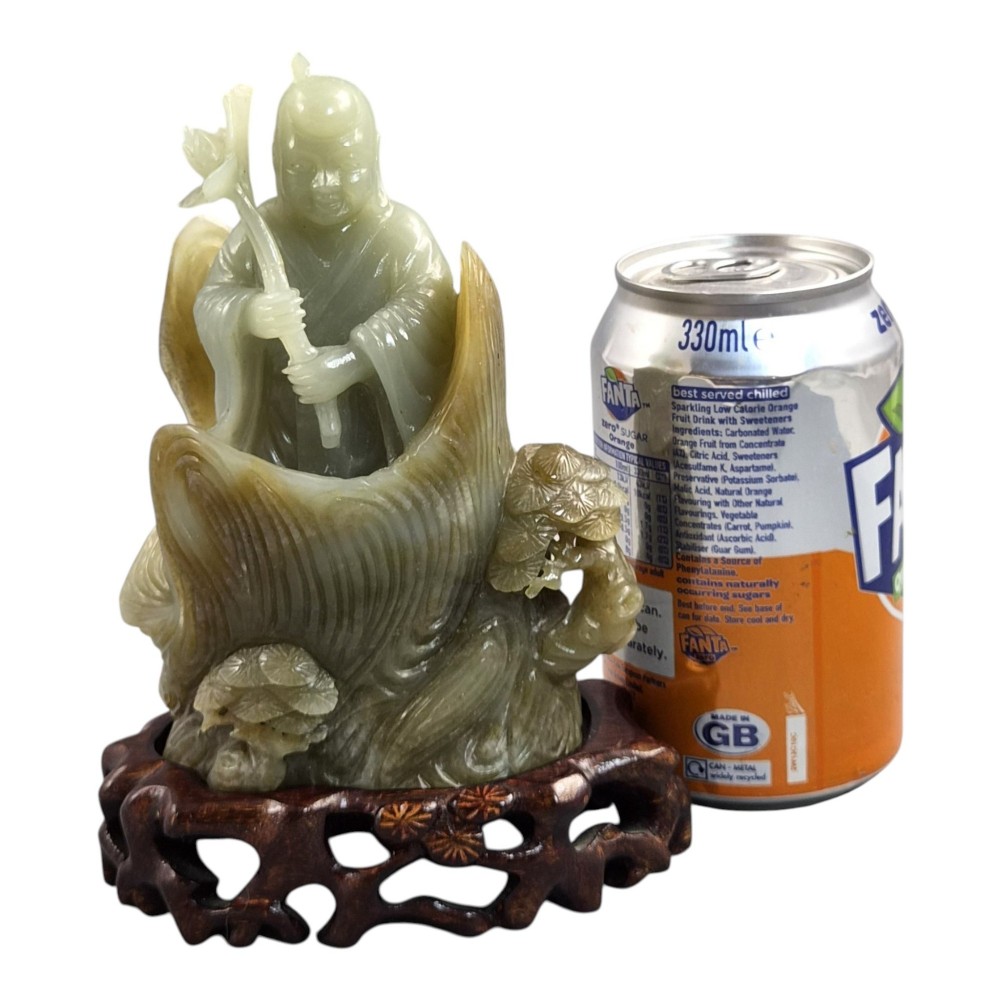 A carved pale green Chinese jadeite figure holding a lotus stem, resting on a fitted dark carved wooden stand. View XII