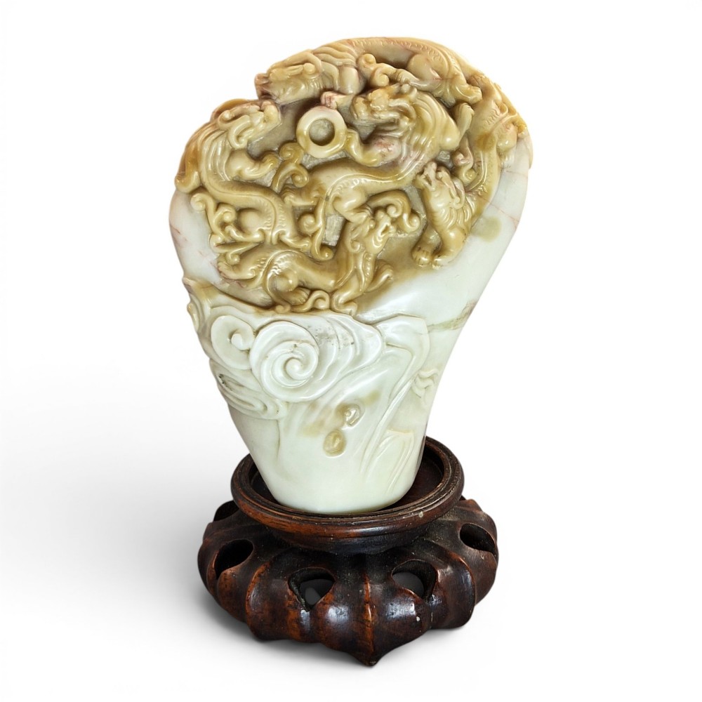 A carved cream and tan Shoushan stone sculpture depicting a dragon amongst clouds set upon a dark turned wooden base.