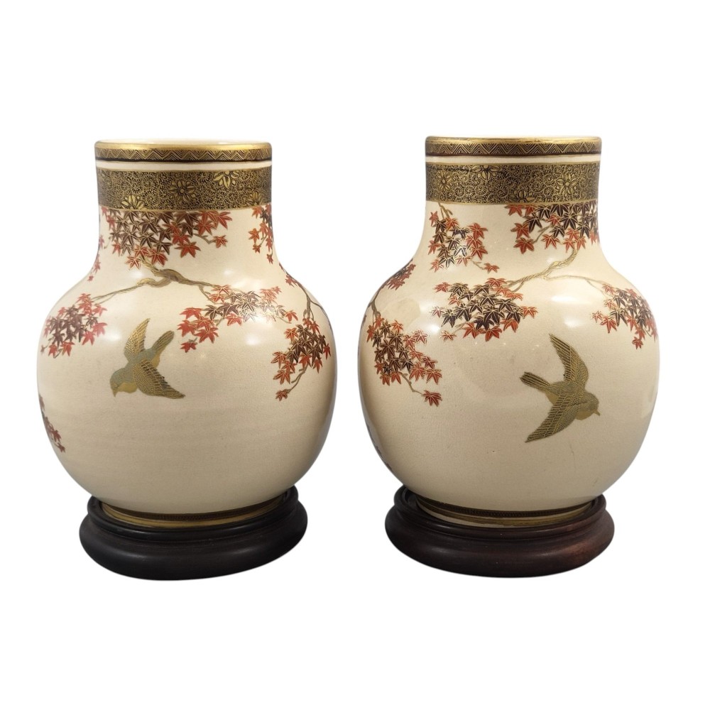 A pair of bulbous cream-coloured Japanese Satsuma earthenware vases decorated with gilt birds and autumnal foliage on dark carved wood stands. View II
