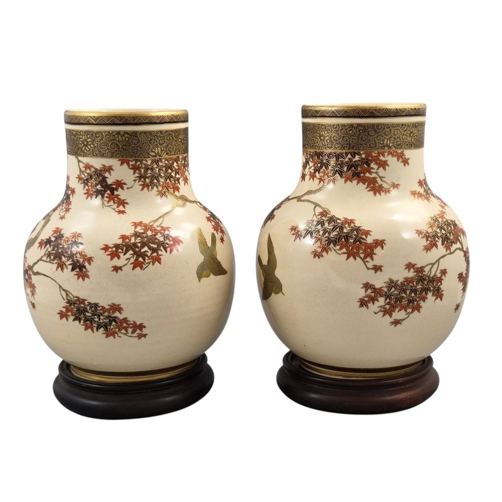 A pair of bulbous cream-coloured Japanese Satsuma earthenware vases decorated with gilt birds and autumnal foliage on dark carved wood stands. View III
