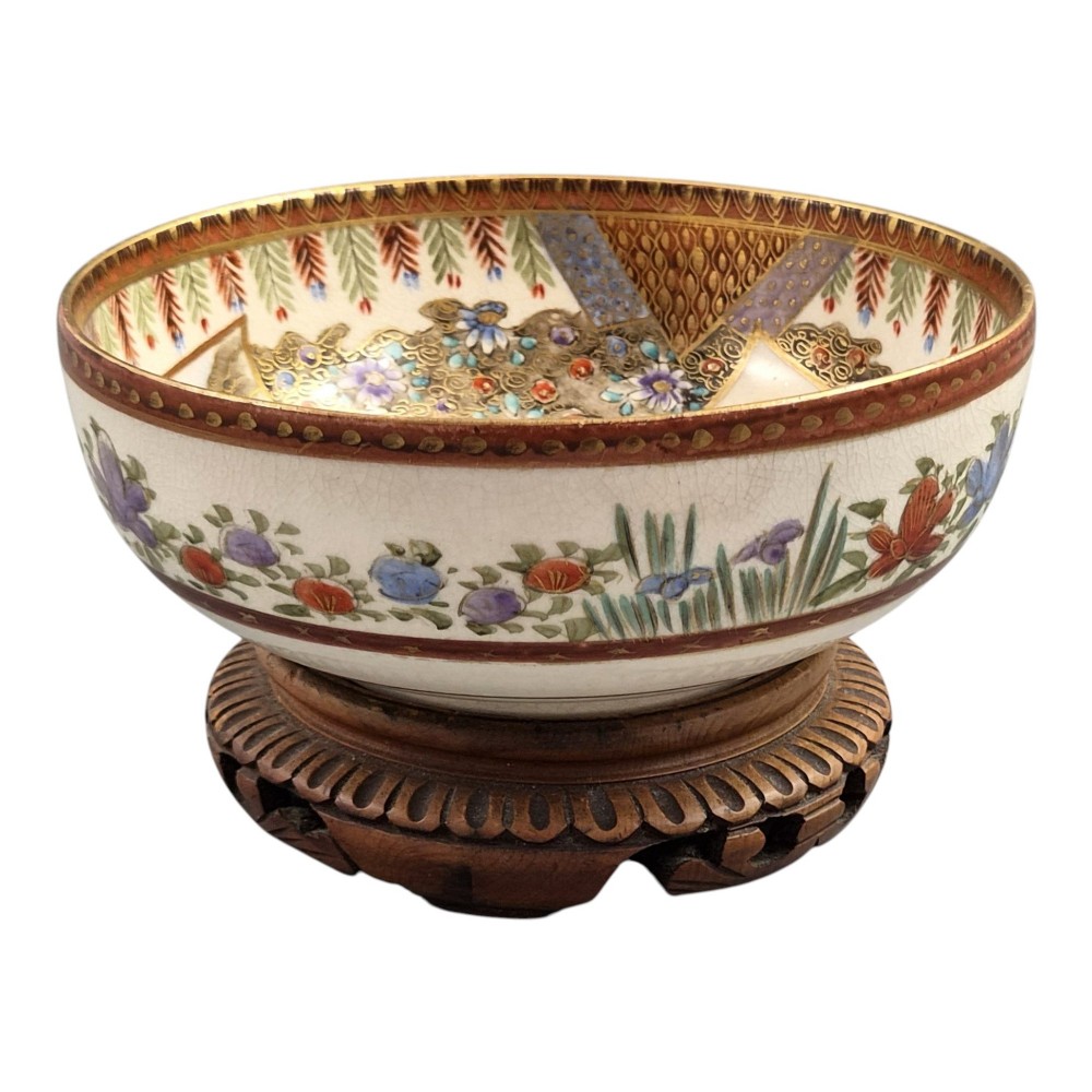An antique Meiji period Japanese Satsuma earthenware bowl featuring hand-painted floral panels and gold detailing, elevated on a carved dark wooden base. View IV