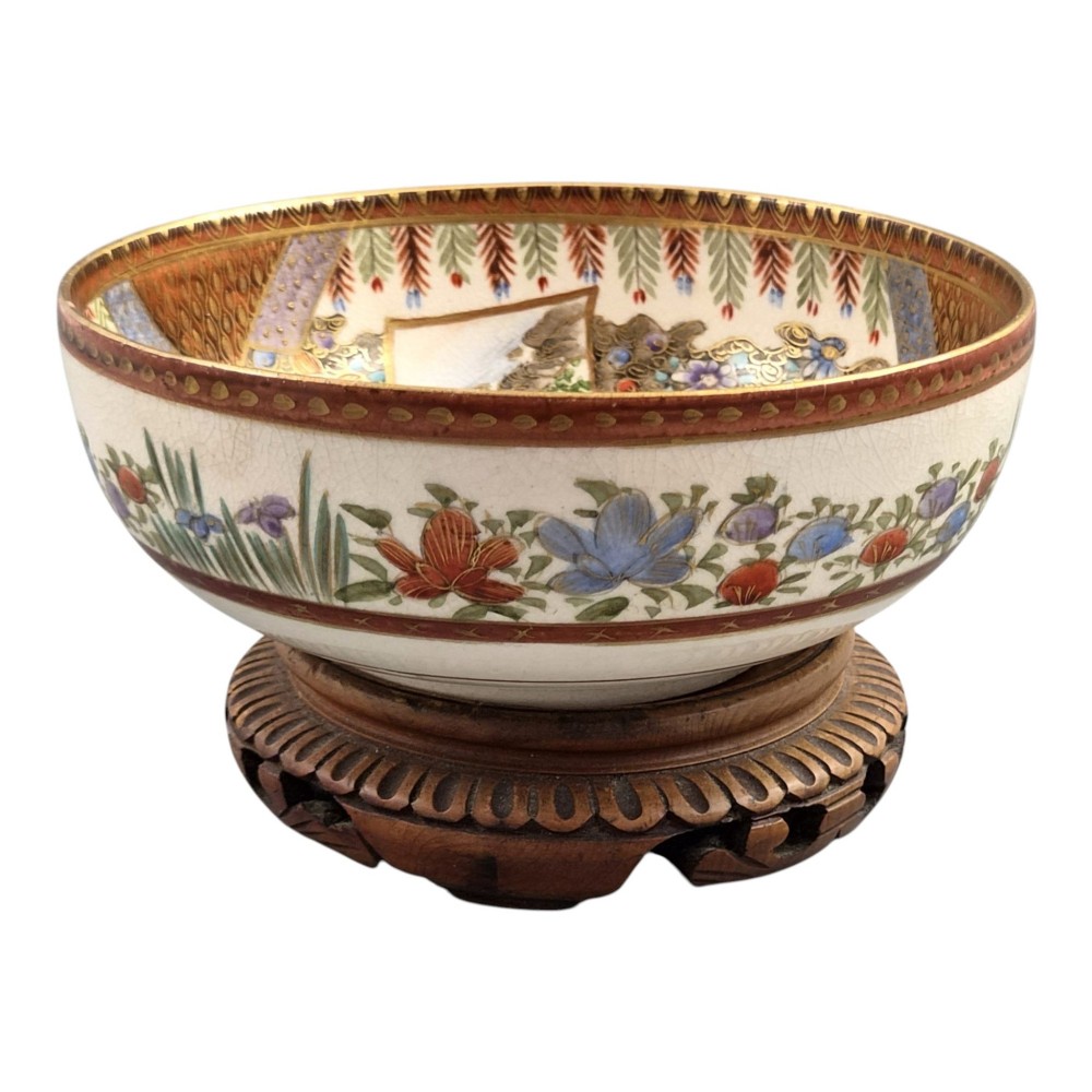 An antique Meiji period Japanese Satsuma earthenware bowl featuring hand-painted floral panels and gold detailing, elevated on a carved dark wooden base. View V